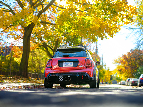 Toronto, Ontario, Canada- October 28, 2023.  Chili red colour MINI COOPER on the streets of Toronto East side, Canada. Fall colours on the trees in the city.  This is the third generation model F56 JCW, since BMW took over iconic brand of MINI. MINI featured in the photo is John Cooper Works model, the most powerful 2 door version. For the first time, this compact car features engine build and designed by BMW, and packs even more power and torque than previous models since 2002 to present. Original design clues and themes are still present on this brand new model. Mini has been around since 1959 and has been owned and issued by various car manufacturers.