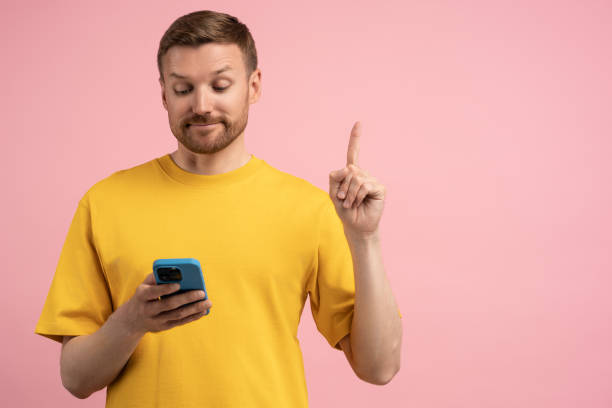 istock Satisfied man raising finger up have creative idea look on cellphone isolated on pink studio blank 1765677612