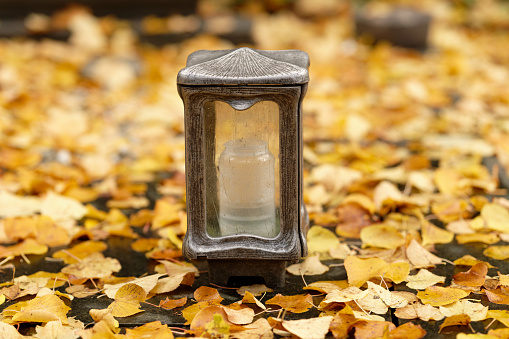 a grave lantern on a grave covered with autumn leaves in a cemetery in autumn