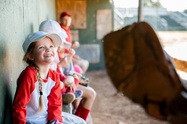 In the dugout, six elementary school students clad in baseball team uniforms are seated
