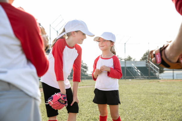 istock Two young girls in baseball uniforms talk while another player and their coach looks on 1765702254