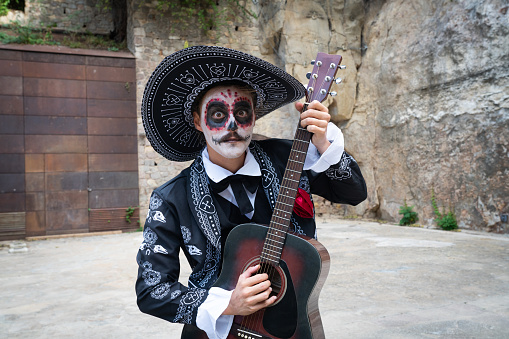 Young man dressed as catrin for day of the dead cellebration playing the guitar