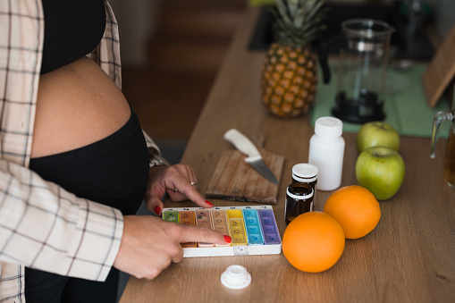 Close-up of a pregnant woman using weekly pill organizer for her prenatal vitamin supplements