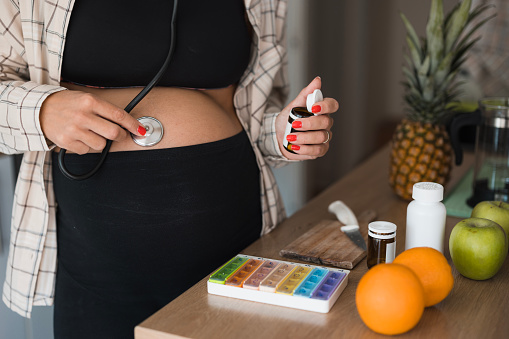 Close-up of pregnant female doctor using stethoscope at home