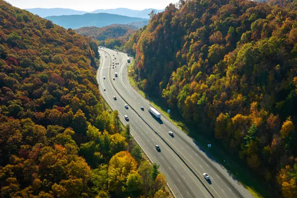 Photo of View from above of I-40 freeway route in North Carolina leading to Asheville thru Appalachian mountains with yellow fall woods and fast moving trucks and cars. Interstate transportation concept