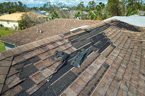 Wind damaged house roof with missing asphalt shingles after hurricane Idalia in Florida. Repair of home rooftop concept.