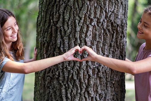 two girls in the forest holding a heart in their hands in front of a tree and laughing