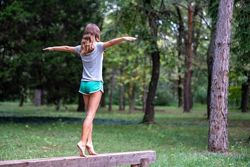 a girl walks alone with outstretched arms on a beam in the forest