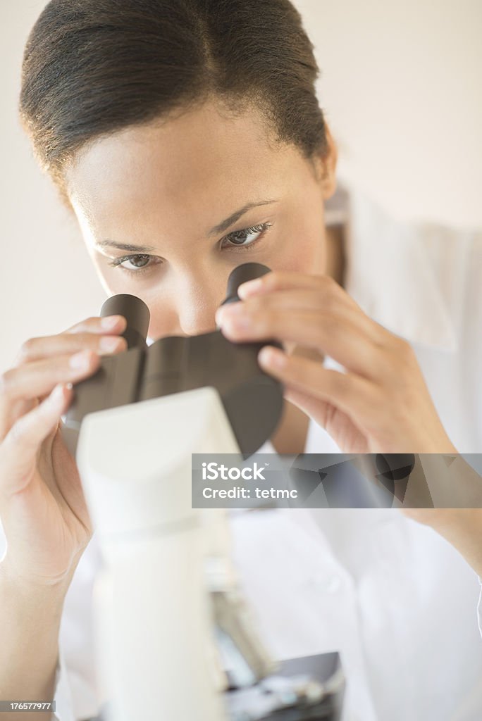 Investigadora mirando a través de un microscopio en los análisis de laboratorio - Foto de stock de 25-29 años libre de derechos