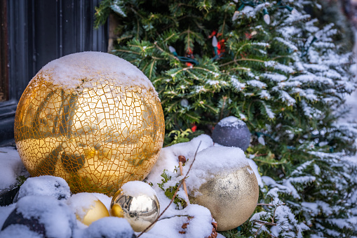 Gold Christmas balls, ornaments and winter holidays decorations covered in snow on window sill, with snowy tree in the background, Petit-Champlain District, Quebec City, Canada (December 2022).
