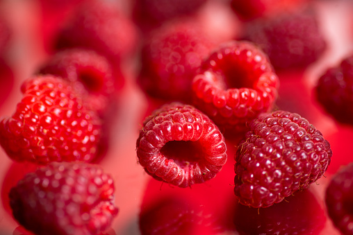Falling ripe juicy raspberries on red background. Closeup