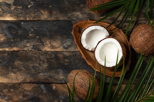 Fresh coconut in bowl, with green leaves on wooden background. With copy space. Healthy food concept