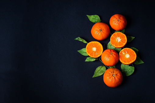 Whole tangerine and halves of ripe fresh fruit with leaves on dark background. With copy space