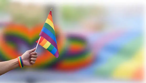 Rainbow flags, LGBT symbol, raising with blurred rainbow wristband background, concept for celebrations and campaign of LGBTQ+ people and respect gender diversity in pride month around the world.