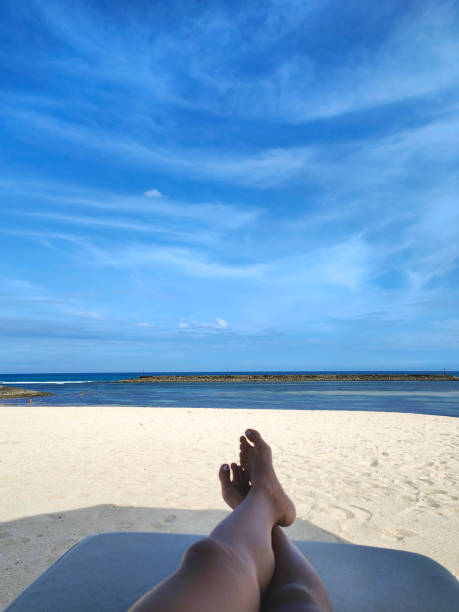 Unrecognizable Woman Legs Crossed at Ankle Lying on Sun Lounger at beach Close-up POV shot of unrecognizable woman legs crossed at ankle Lying on Sun Lounger at empty beach legs crossed at ankle stock pictures, royalty-free photos & images