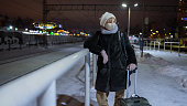 Travel in winter. In the winter cold, snowy night, a mature woman with luggage waits on a railroad platform for a train.