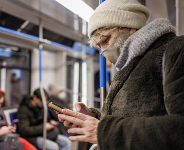 korzystanie ze smartfona w metrze podczas pandemii. dojrzała kobieta nosząca maskę ochronną na twarz dla bezpieczeństwa publicznego jadąca pociągiem wypełnionym ludźmi. - unrecognizable person human face large group of people crowd zdjęcia i obrazy z banku zdjęć