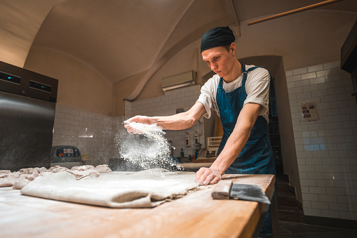 Caucasian artisan baker working in a small bakery. Sprinkling flour on a bakers couche before handcrafting baking goods.