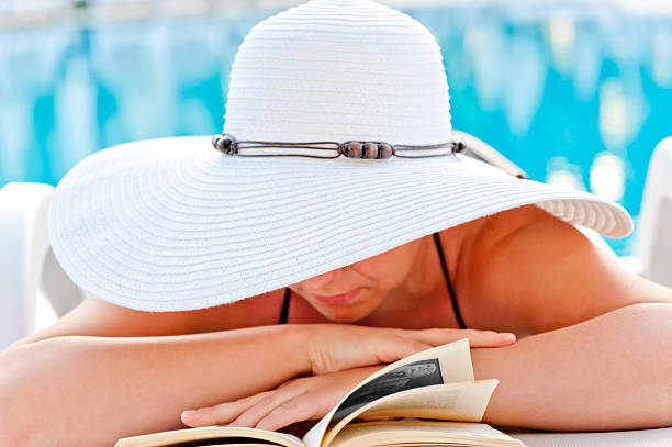 istock girl in a white hat reading book by the pool 176600158