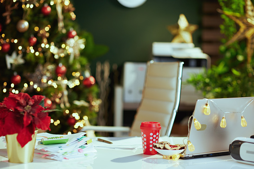 modern Christmas decorated green office with laptop, poinsettia, Christmas beverage and cookies.