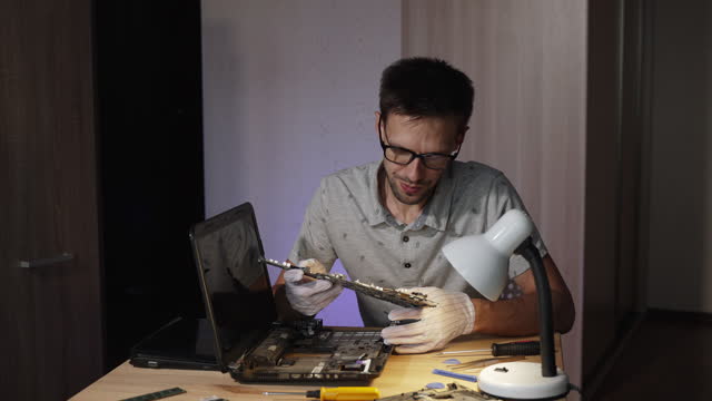 Repairman in glasses with frustrated look examines motherboard of laptop.