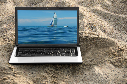 A laptop computer on a sandy beach.  Sailboat scene on the screen. The boat image is mine.
