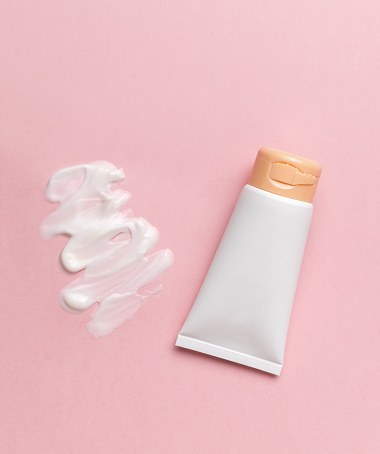 A white tube and smeared cream on a pink background. The concept of body care. Flat lay.