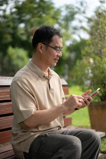 istock A happy retired Asian man using his smartphone, texting someone while sitting on a bench in a park. 1766143316