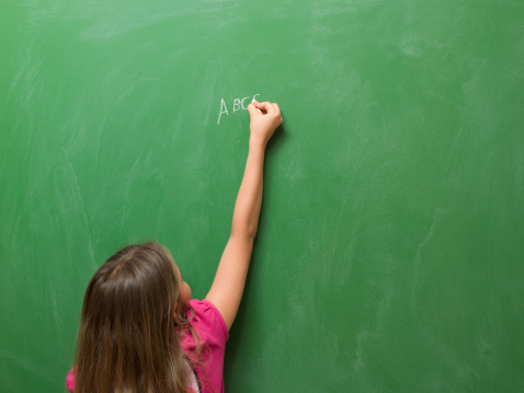 Little girl writing abc on blank blackboard