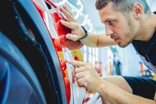 The process of installing protective film on the new red car.
