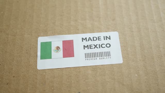 Hands applying MADE IN MEXICO flag label on a shipping box with product premium quality barcode. Manufacturing and delivery. Product factory import and export.