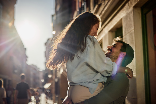 Cheerful man having fun while holding his girlfriend on the city street.