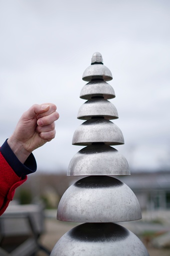 An individual hand knocking a set of bells positioned outdoors.