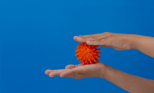 Child hands rolling spiky orange massage needle ball between palms over blue background