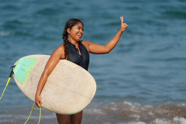 Indonesian Female Surfer Walking Out of Water after Surfing Carrying Surfboard stock photo