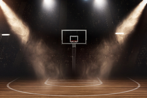 An atmospheric basketball court, bathed in the dramatic interplay of light and shadow, stands ready for action. The intense beams of light pierce through the haze, illuminating the hoop as if highlighting the epicenter of an impending showdown. A captivated audience fades into the dark, their eager anticipation palpable, awaiting the players to take center stage.