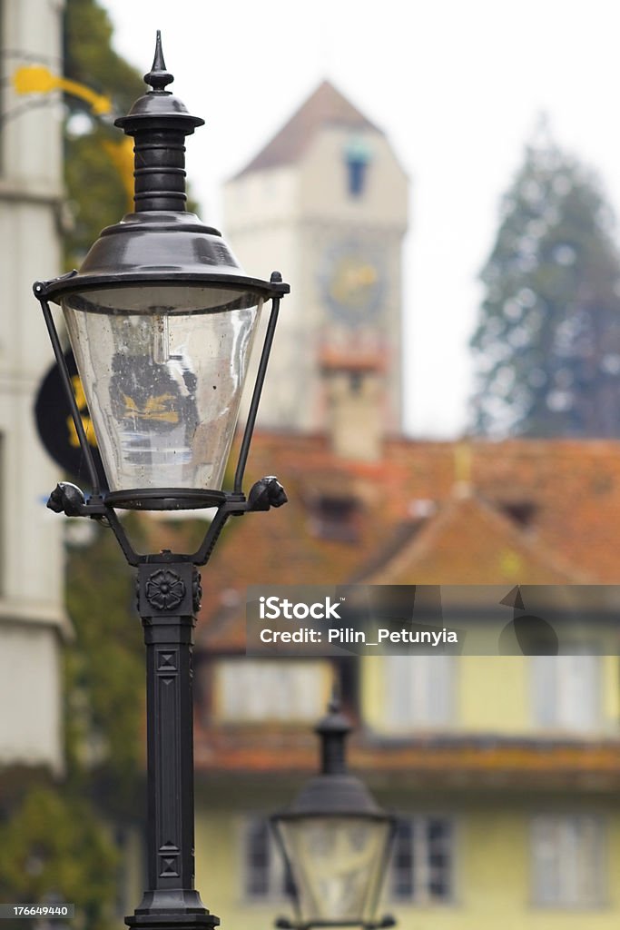 street lamps against background of ancient tower, Lucerne. The image with a focus on old street lamp with reflecting day light. In the background the city clock tower. Lucerne. Ancient Stock Photo