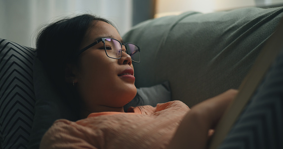 istock Young single woman wearing glasses reading a book on comfortable sofa. 1766507342