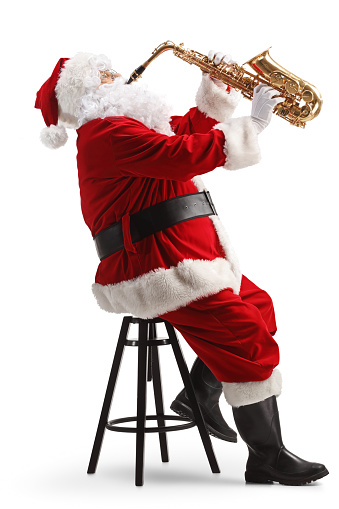 Full length profile shot of Santa Claus sitting on a chair and playing a saxophone isolated on white background