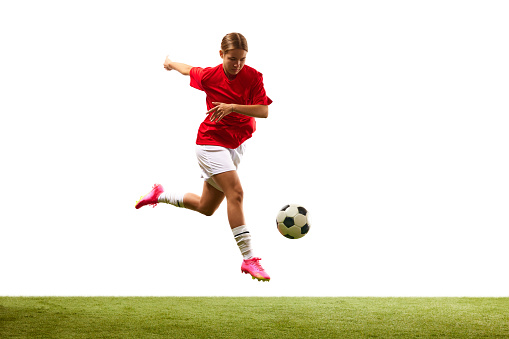 Dynamic image of young girl, football player in motion during game, hitting ball in a jump isolated on white background. Concept of sport, competition, action, success, motivation. Copy space for ad
