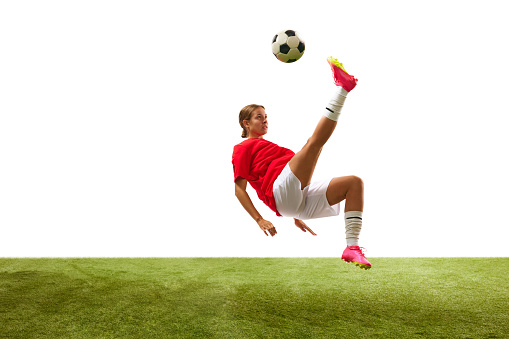 Young woman, female football player in motion, hitting ball with leg and falling sown in grass isolated on white background. Concept of sport, competition, action, success, win. Copy space for ad