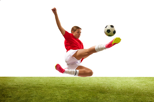 Dynamic image of young girl, football player training, hitting ball in jump isolated on white background. Concept of sport, competition, action, success, motivation. Copy space for ad
