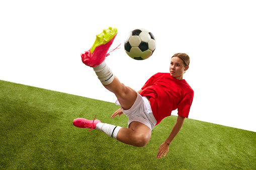 Concentrated female football player in motion, hitting ball and falling down during game in grass field isolated on white background. Concept of sport, competition, action, success. Copy space for ad