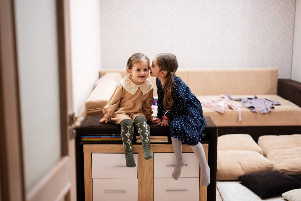 Two sisters sit on the sofa and tell and share girlish secrets with each other.