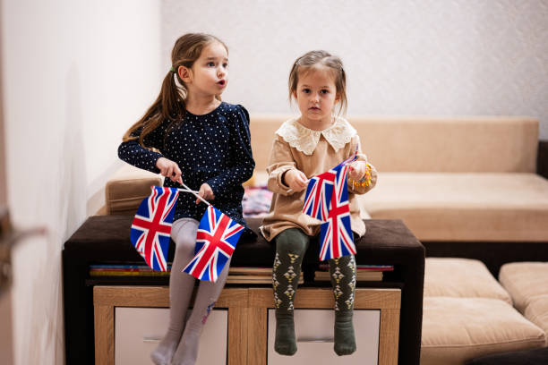 istock Two sisters are sitting on a couch at home with british flags on hands. Great Britain children girls with flag . 1766533532