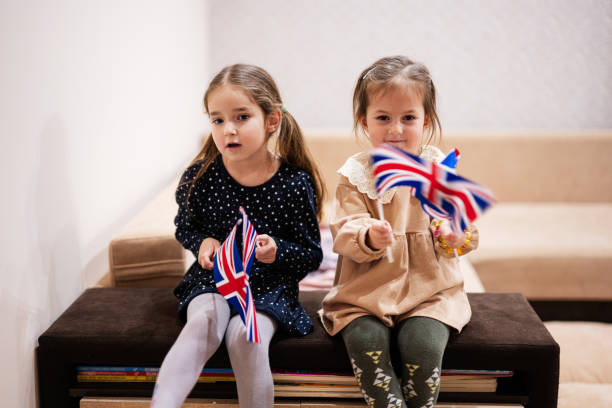 istock Two sisters are sitting on a couch at home with british flags on hands. Great Britain children girls with flag . 1766534610