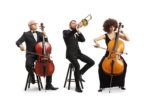 Full length portrait of musicians sitting and playing cellos and a trombone isolated on white background