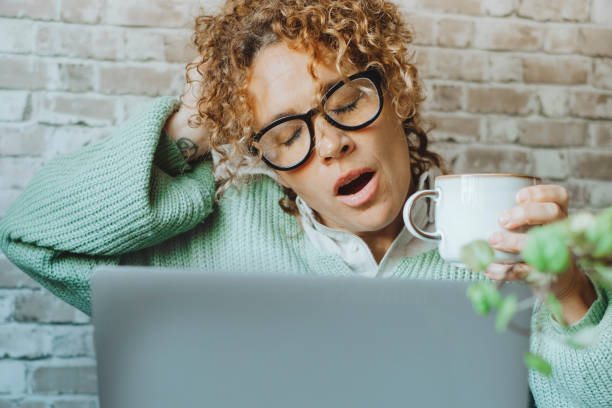 Tired woman suffering insomnia working in front of. a laptop computer and drinking coffee for caffeine. Concept of overwork condition. Home office job business genale people doing yawn alone. Online stock photo