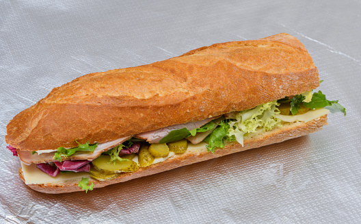 Isolated folded baguette sandwich with ham, cheese and lettuce closeup