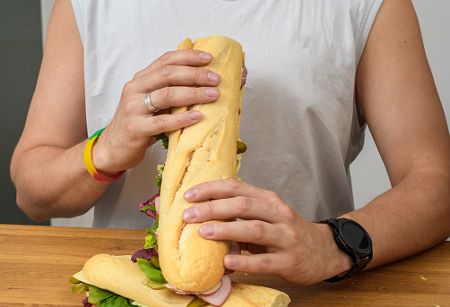 A man eats a baguette sandwich with ham, cheese and lettuce for breakfast closeup